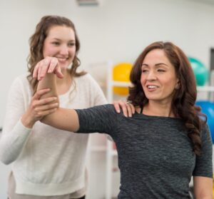 Woman in her 50s doing a shoulder exercise with a physical therapist to relieve shoulder pain.